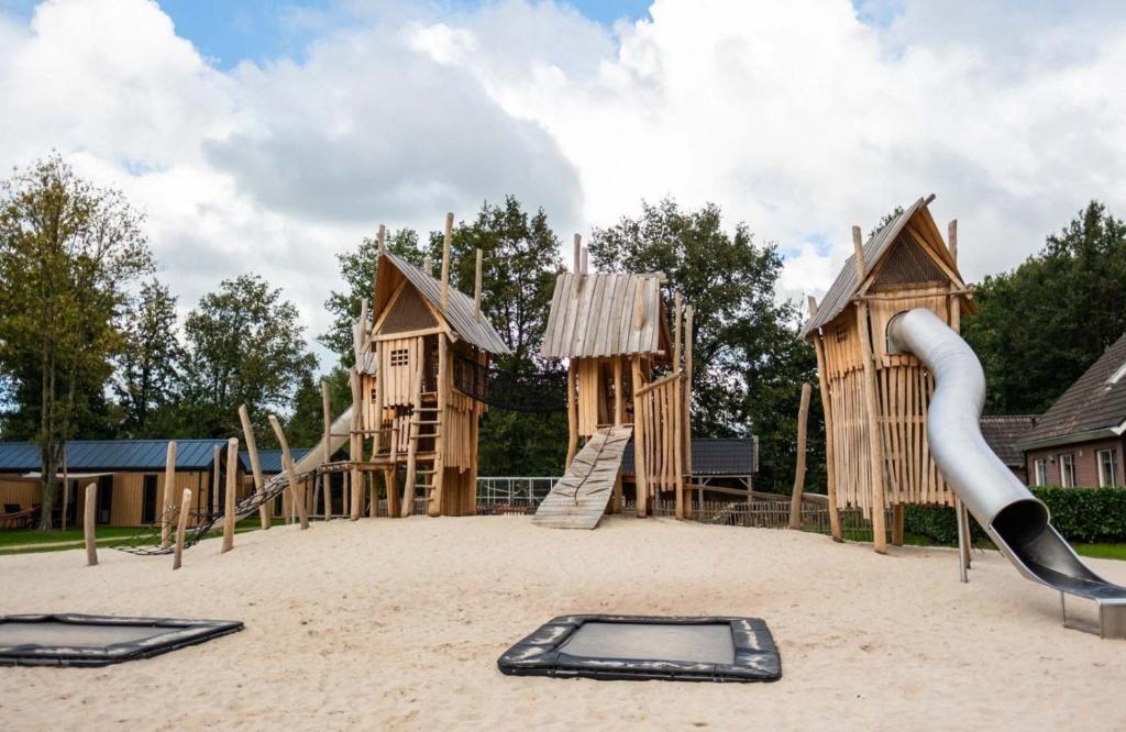 a playground with wooden play equipment in the sand at Vakantiehuisje op 5 star kindercamping in Mariënberg