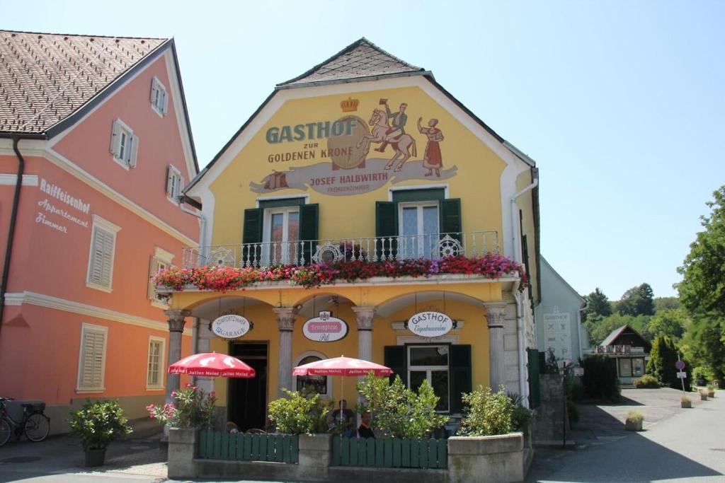 a yellow building with a balcony with red umbrellas at Zur goldenen Krone in Ehrenhausen