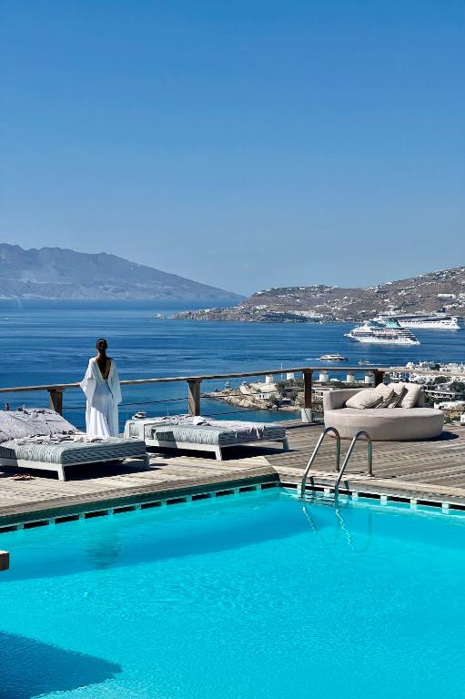 a woman standing on a deck next to a swimming pool at Tharroe of Mykonos Boutique Hotel in Mikonos
