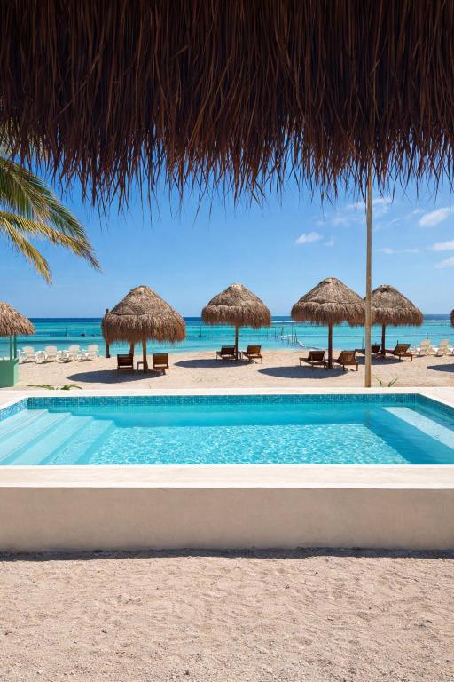 ein Schwimmbad mit Strohschirmen am Strand in der Unterkunft Oneiro Suites with Sea View in Mahahual