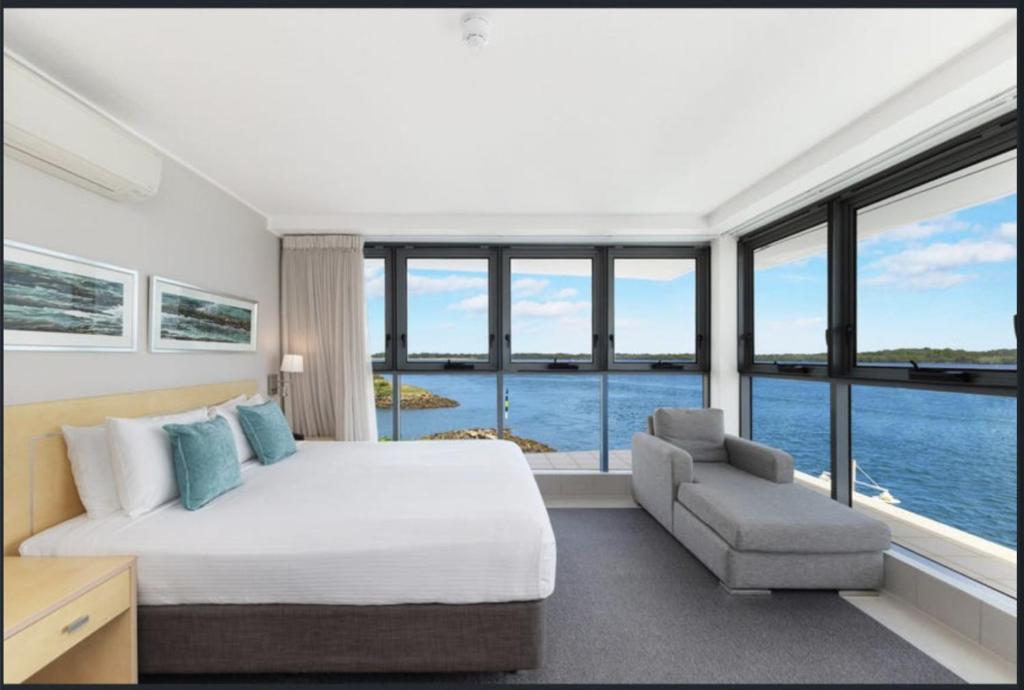 a bedroom with a bed and a chair and windows at River's Edge Premium Retreat in Ballina