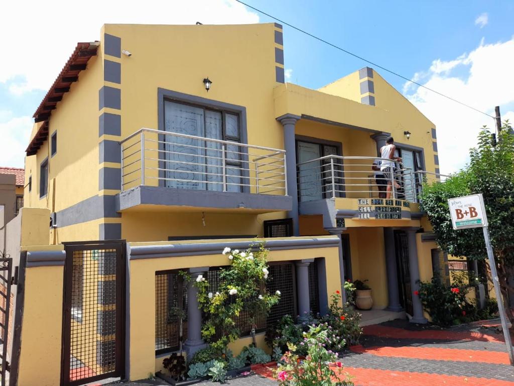a man standing on the balcony of a yellow house at THE ROSE BnB in Soweto