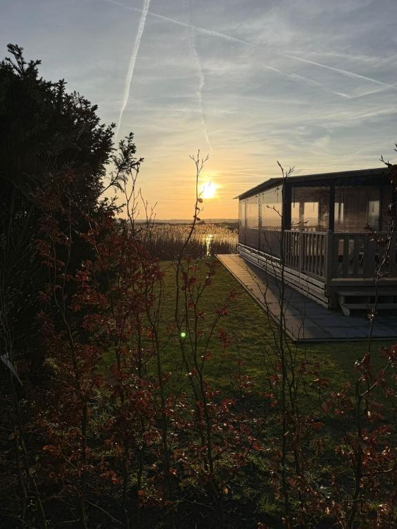 a house with the sun setting in a field at Het mooiste plekje van het park in Kropswolde