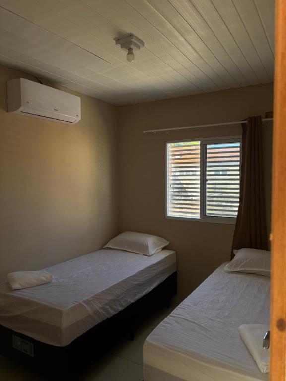 zwei Betten in einem kleinen Zimmer mit Fenster in der Unterkunft Flat in Japaratinga