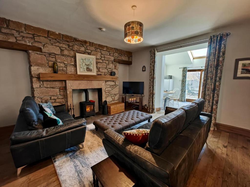a living room with leather furniture and a stone wall at 3 Bed in Aviemore oc-s30815 in Aviemore