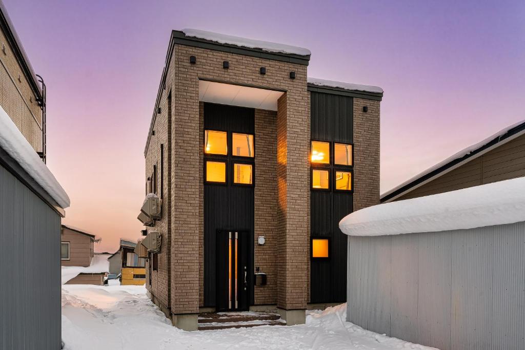 a brick house with illuminated windows in the snow at Astage Villa Kamifurano in Kami-furano