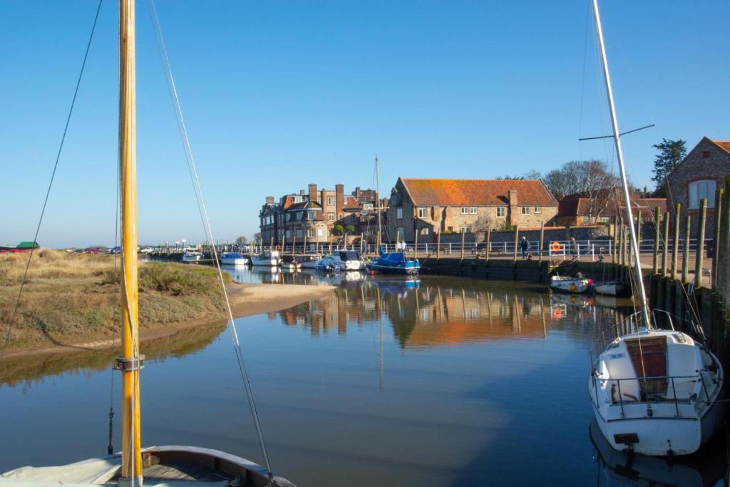 two boats are docked in a river with houses at 2 Bed in Blakeney oc-1977 in Blakeney