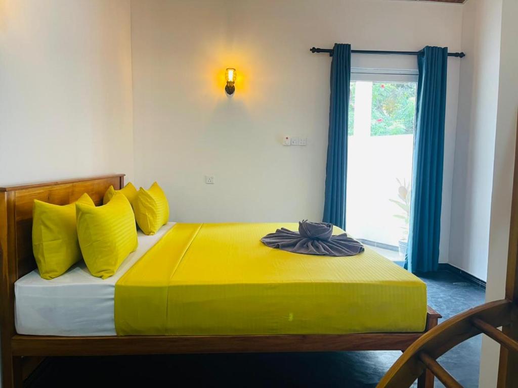 a bedroom with a bed with yellow pillows and a window at Hasara Homestay in Dickwella
