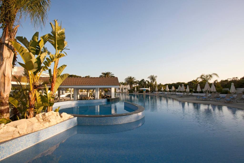 a pool at a resort with palm trees and chairs at Christofinia Hotel in Ayia Napa