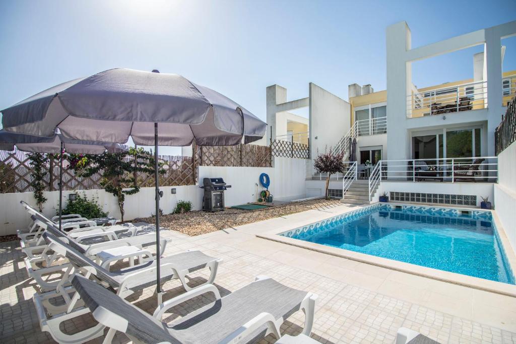 a pool with chairs and an umbrella next to a house at Villa Granada in Almancil