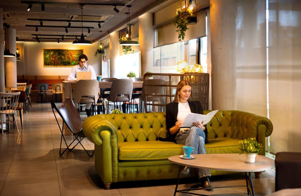 a woman sitting on a green couch in a restaurant at Hotel Bed4U Pamplona in Cordovilla