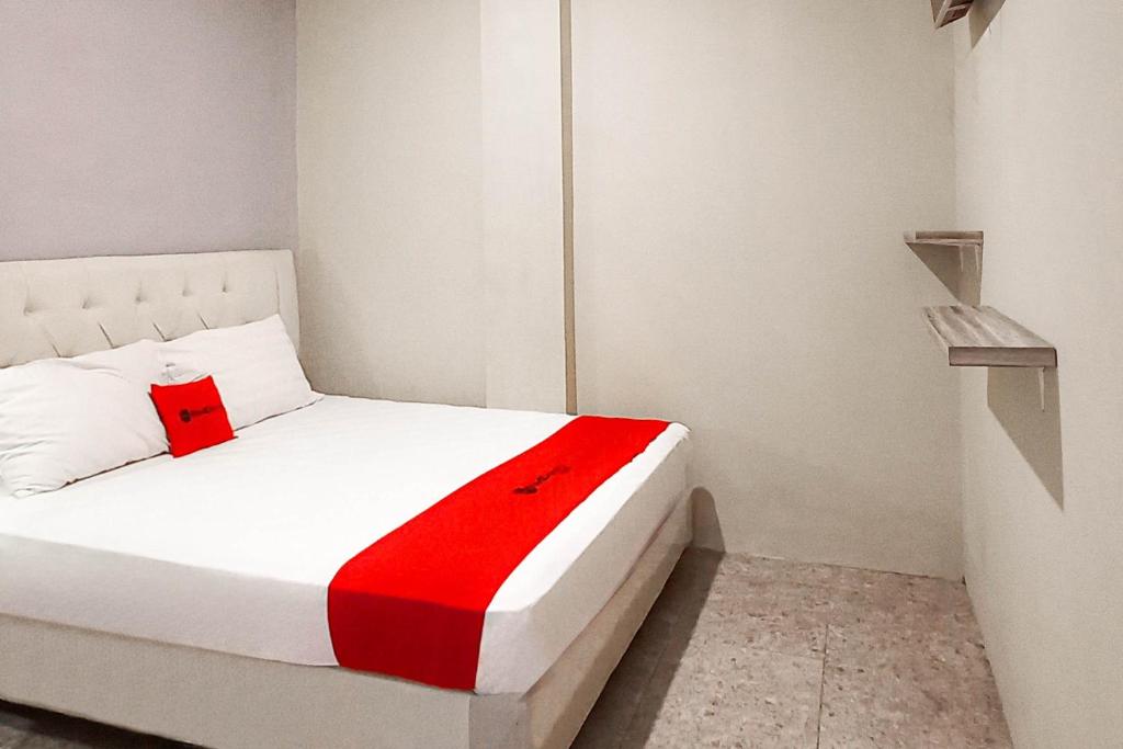 a bedroom with a white bed with a red blanket at RedDoorz at Deluxe Hotel near Terminal Purabaya Bungurasih in Sidoarjo