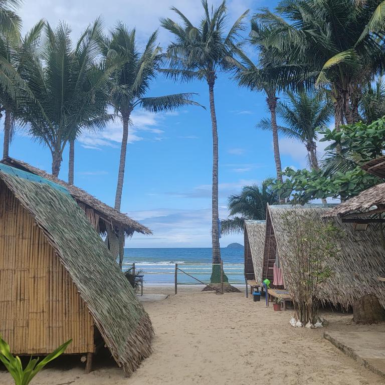 a beach with palm trees and huts and the ocean at Island Crib in El Nido