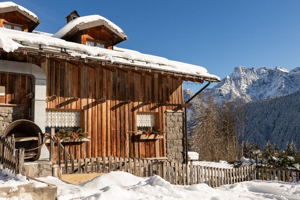 a log cabin in the snow with mountains in the background at Agriturismo Piccola Baita in Falcade