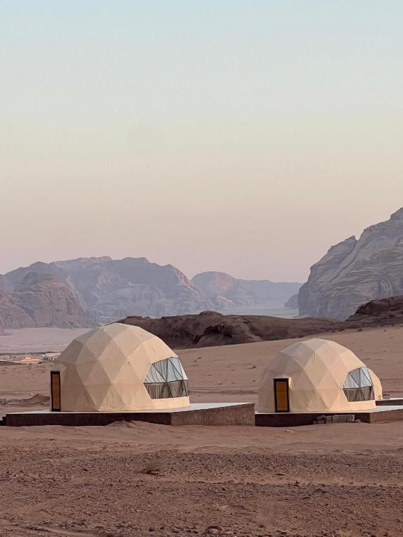 two domes in a desert with mountains in the background at Lawrence Luxury Camp in Wadi Rum