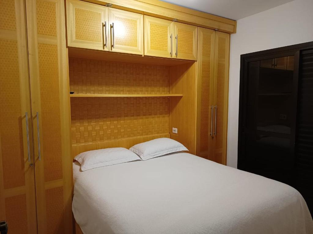a bedroom with a white bed and wooden cabinets at Piemonte Flat Serra Negra in Serra Negra