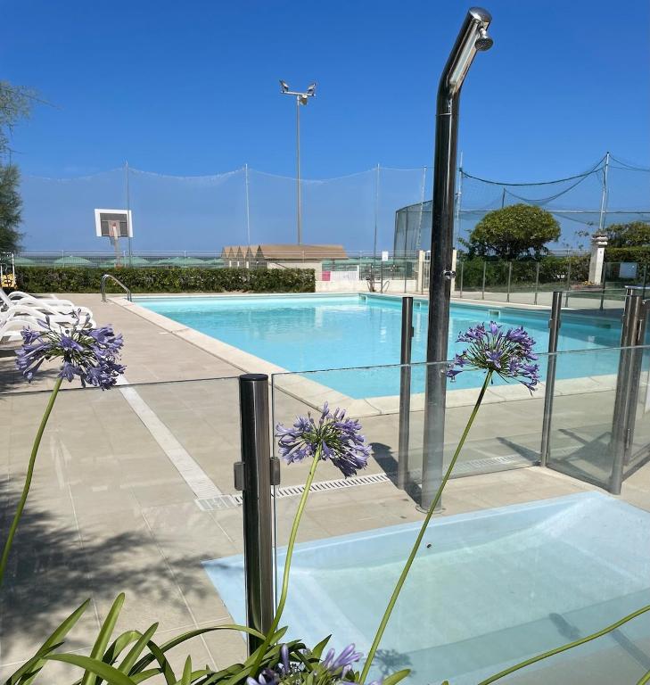 a swimming pool with purple flowers next to a fence at Apartament Mare e Sole z basenem i przy plaży in Marotta