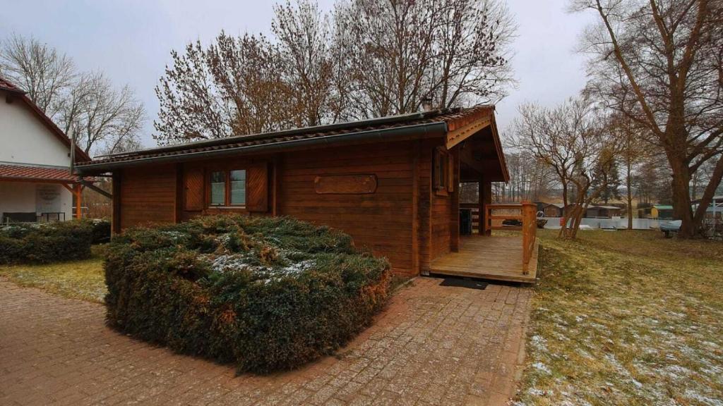 a small wooden house with a porch and a bush at Holzhaus direkt am See in Priepert