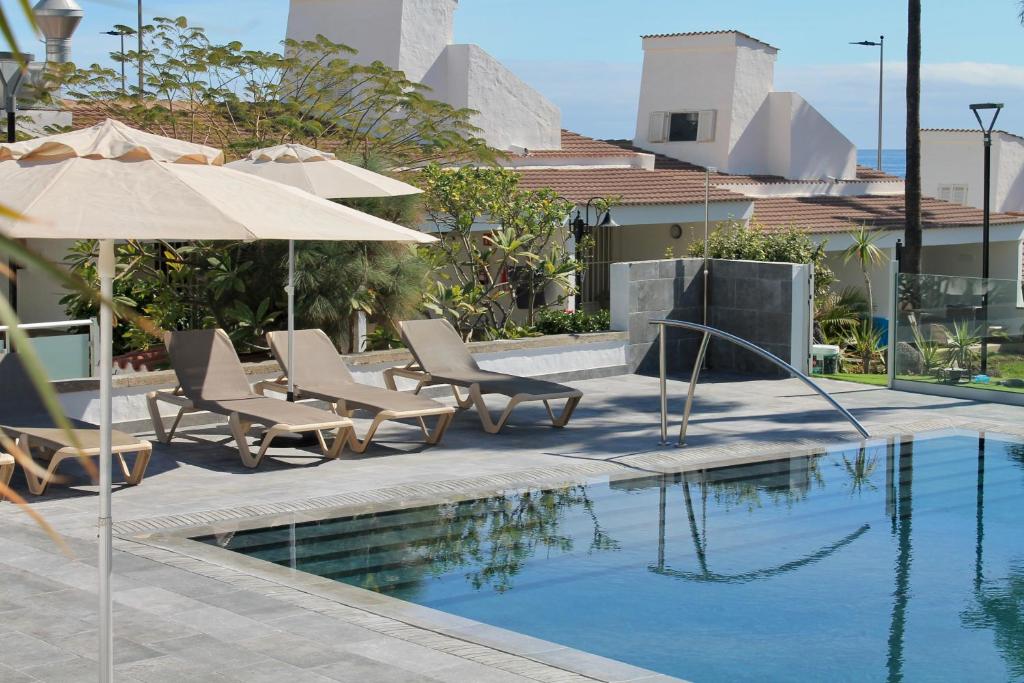 a swimming pool with chairs and umbrellas next to a swimming pool at Makāi Bungalows in Playa del Aguila