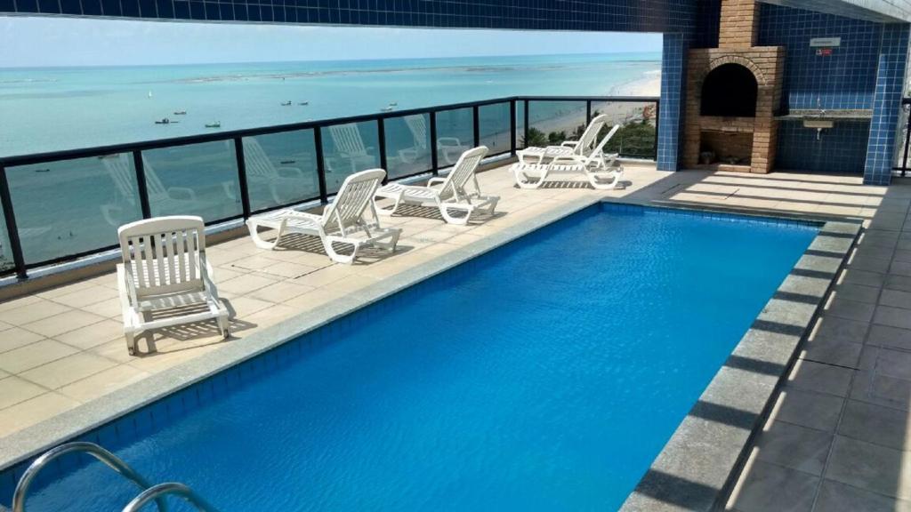 a swimming pool with lounge chairs and the ocean at Apartamento Luxo 2/4 Beira-Mar Pajuçara - Maceió in Maceió