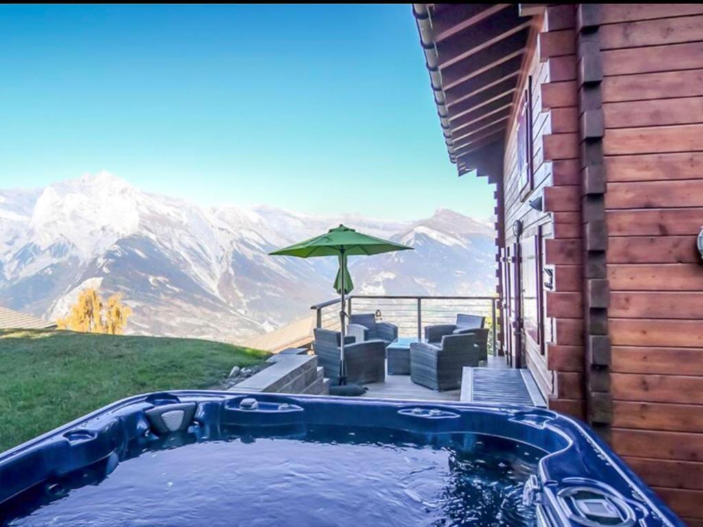 a swimming pool with chairs and an umbrella and mountains at Chalet La Balance by Interhome in Nendaz