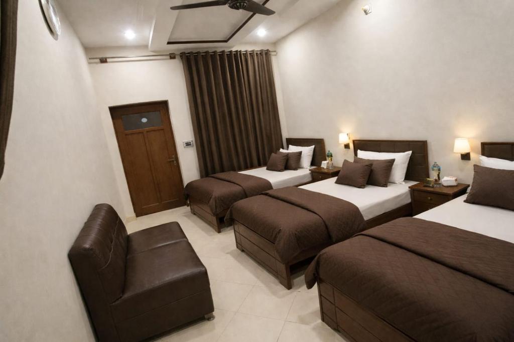 a hotel room with three beds and a chair at Al Huda Hotel in Multan