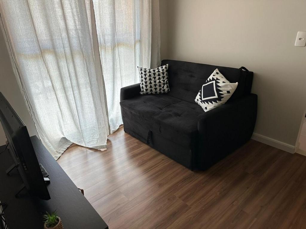 a black couch sitting in a living room next to a window at Apto vista in Ponta Grossa