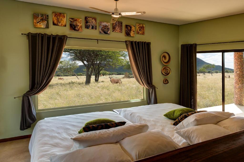 twee bedden in een slaapkamer met uitzicht op een veld bij Okonjima Plains Camp in Otjiwarongo