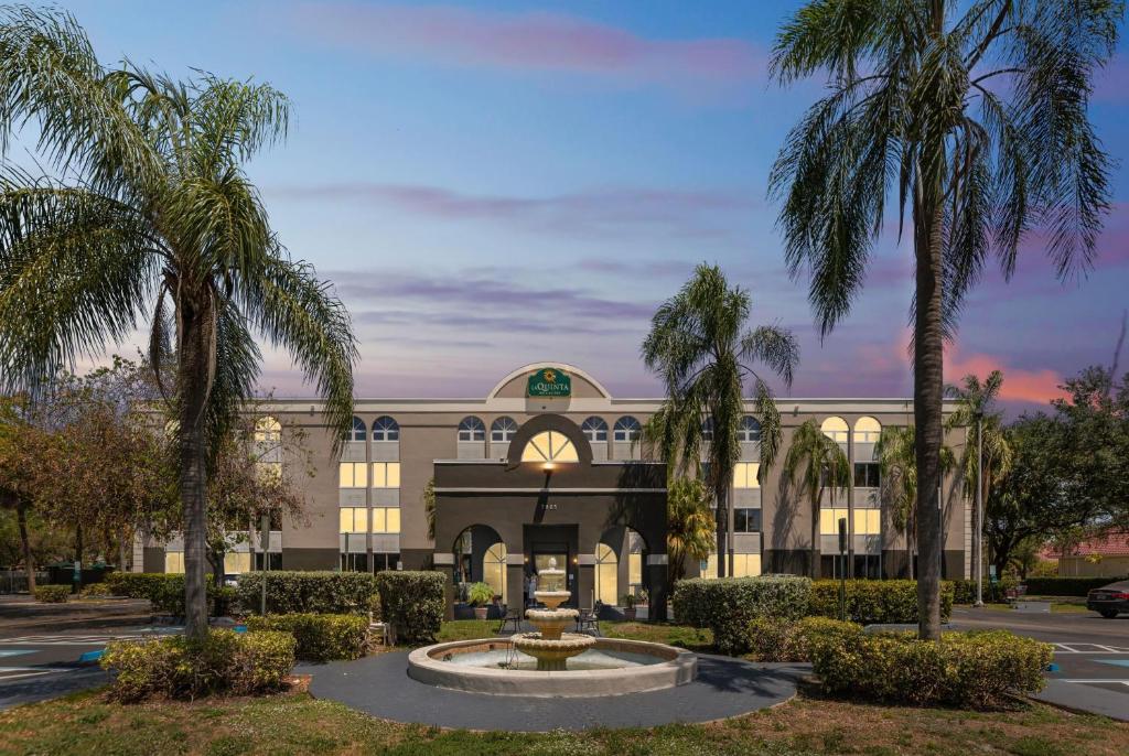 a building with palm trees and a fountain in front at La Quinta by Wyndham Miami Lakes in Miami Lakes