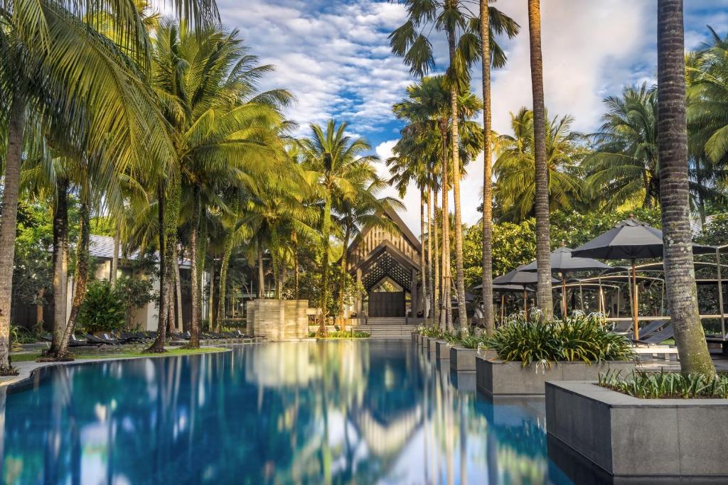 a pool with palm trees in front of a building at Twinpalms Phuket in Surin Beach