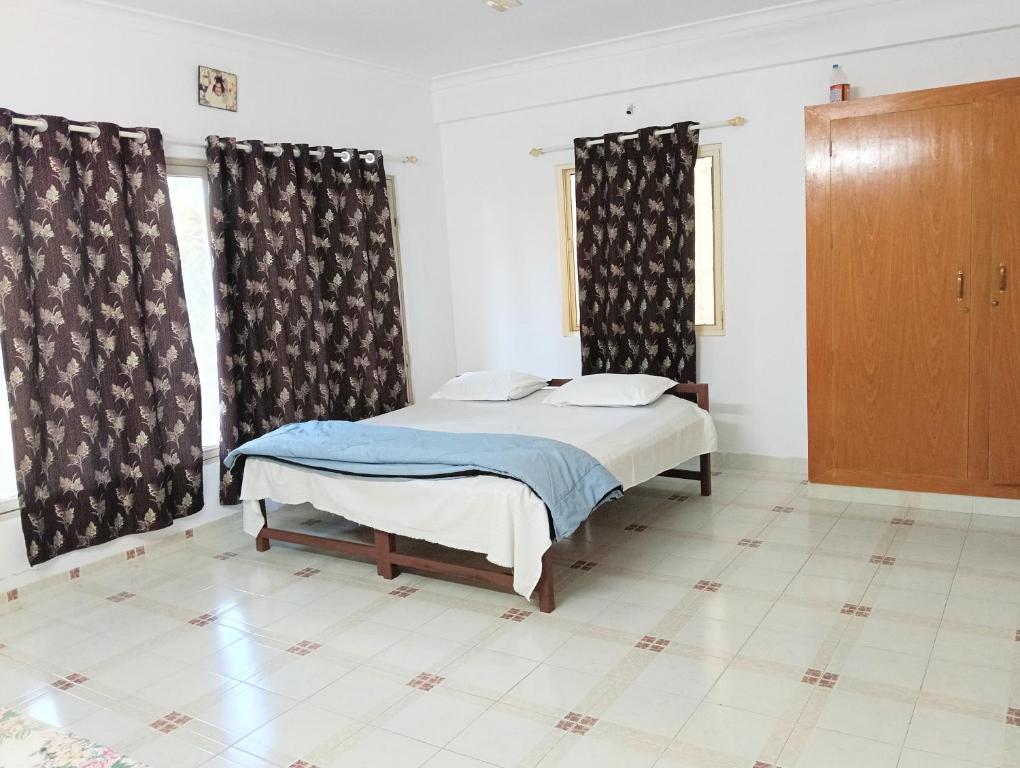 a bedroom with a bed and two windows with curtains at Chetanya Homestay in Puttaparthi