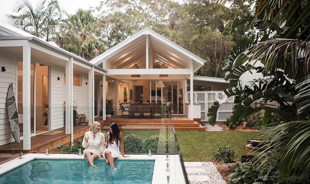 two women sitting on the edge of a swimming pool in a house at Moso House Pearl Beach in Pearl Beach