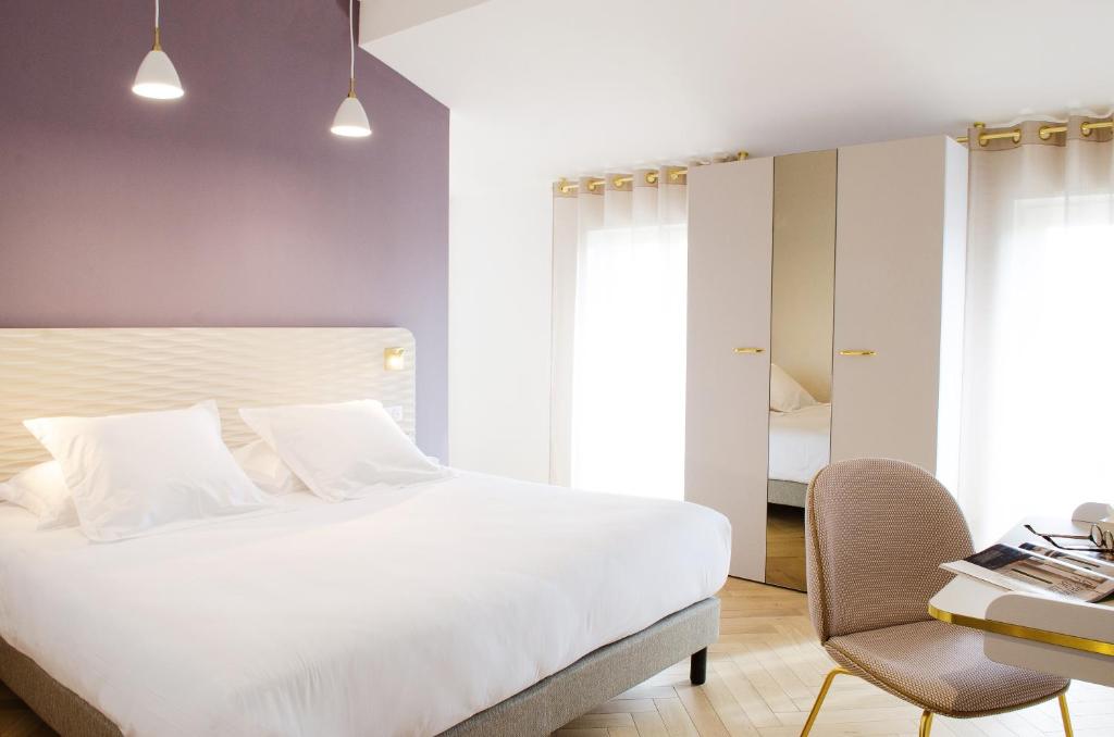 a bedroom with a large white bed and a chair at Hôtel le XIX in Béziers