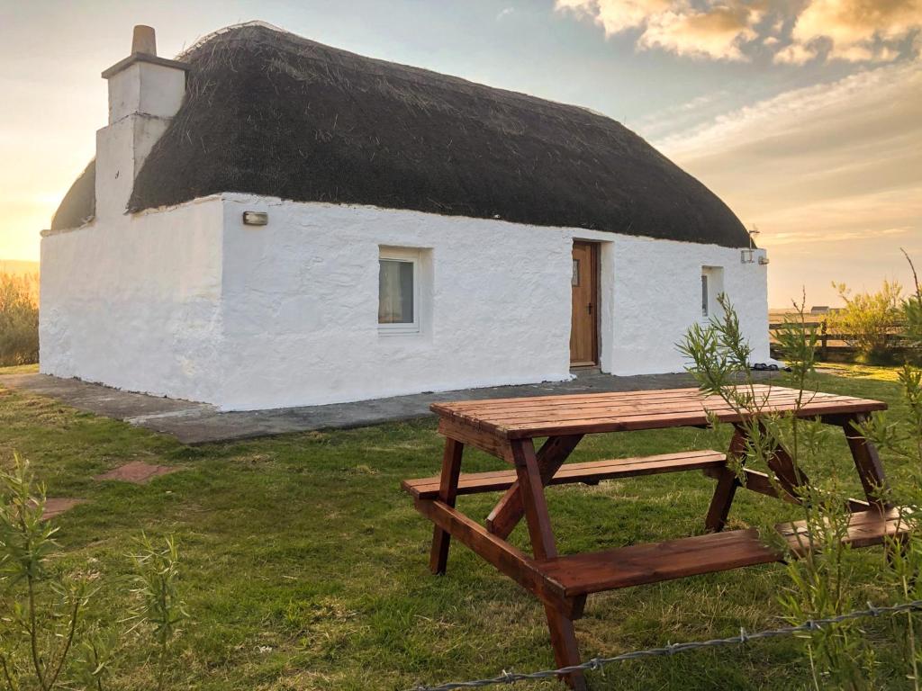 a thatch roofed building with a picnic table in front of it at Taigh Violet Rose in Gramisdale