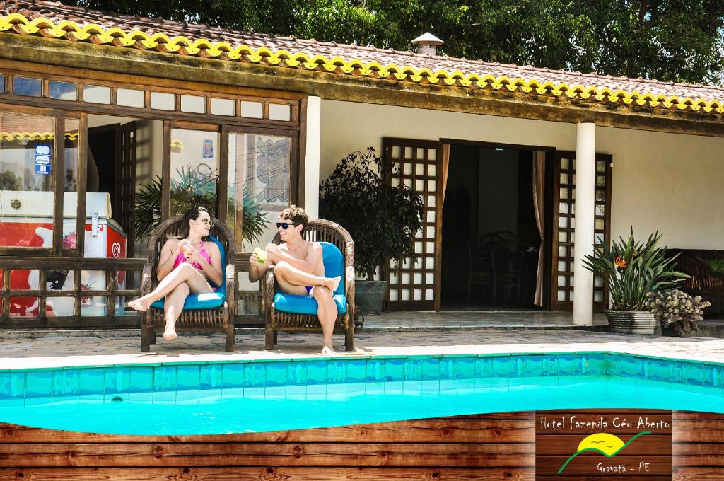 Dos personas sentadas en sillas junto a una piscina en Hotel Fazenda Ceu Aberto, en Gravatá