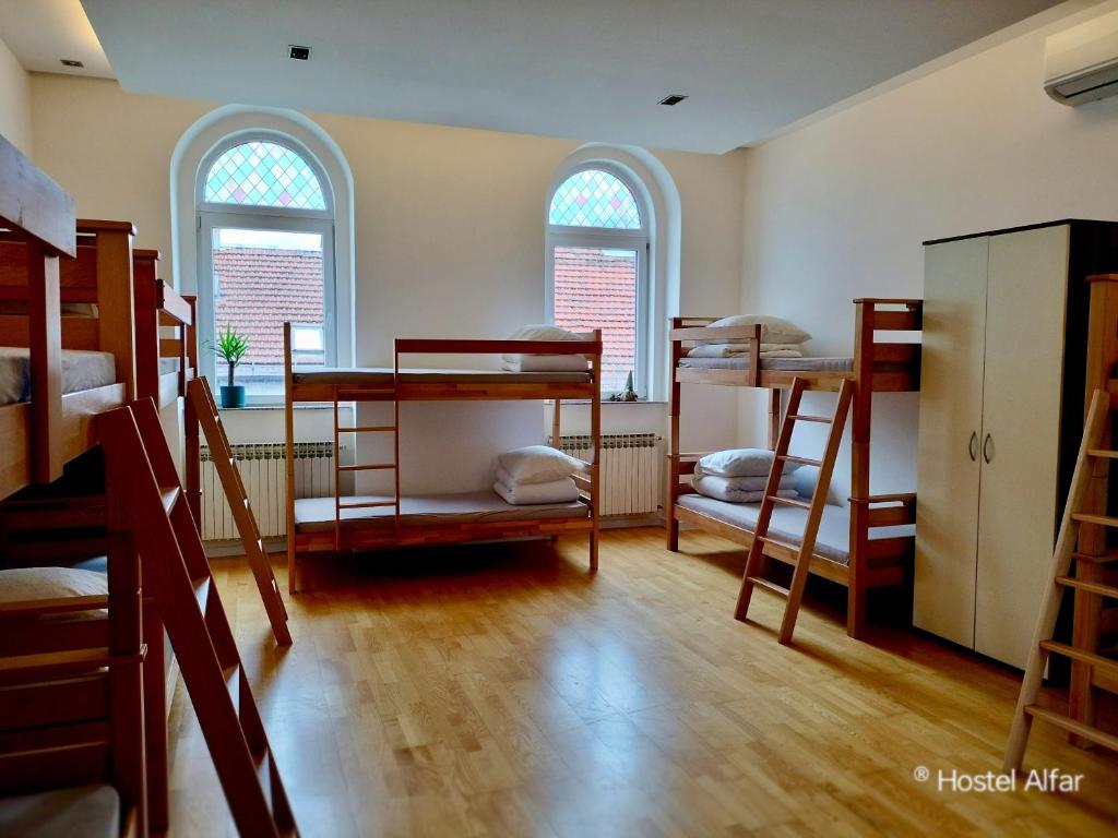a room with several bunk beds and two windows at Hostel Alfar in Sarajevo