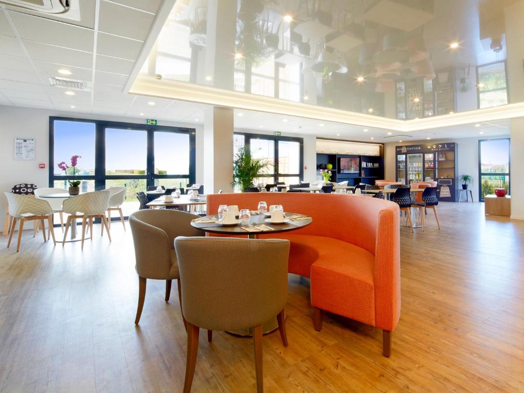 a restaurant with an orange couch and tables and chairs at Kyriad Prestige Residence & Spa Cabourg-Dives-sur-Mer in Dives-sur-Mer
