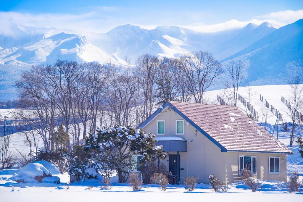 a house in the snow with mountains in the background at North Furano House in Kami-furano