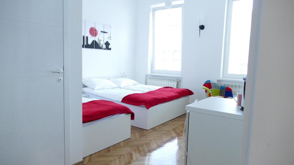 a white bedroom with two beds with red covers at Apartment Mona in Sarajevo