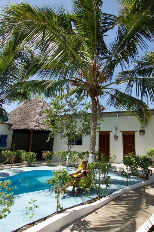 a woman in a bikini sitting under a palm tree near a swimming pool at Green Oasis in Nungwi