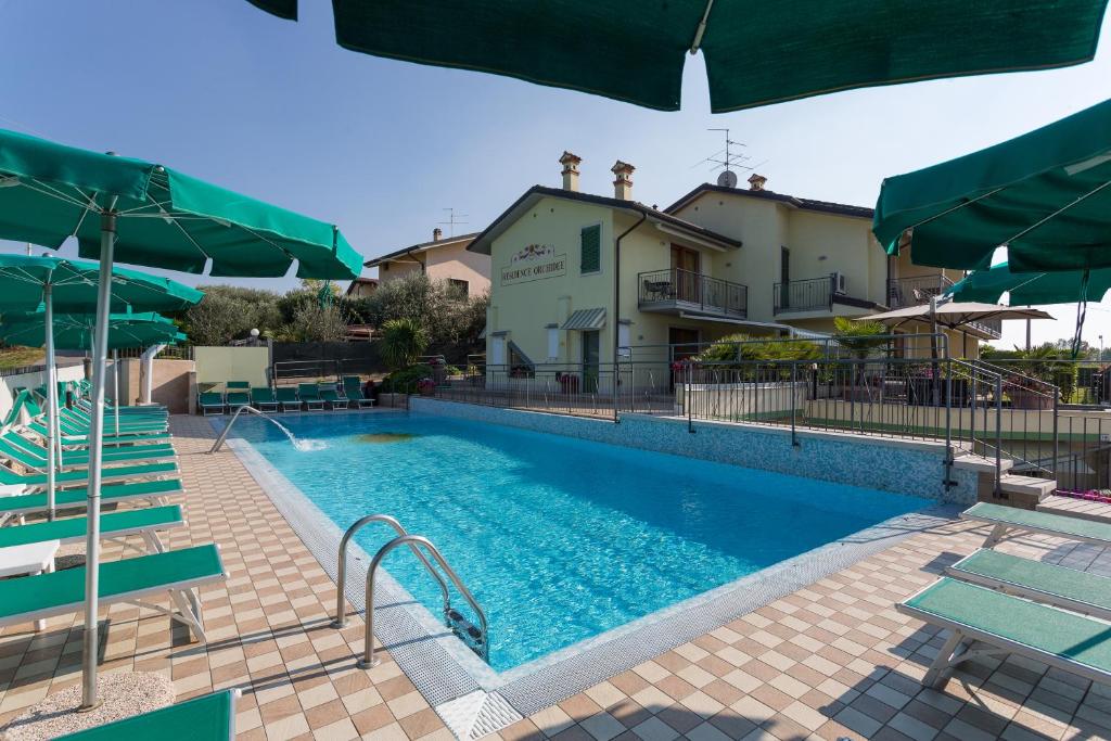 a large swimming pool with chairs and umbrellas at Residenza Orchidee in Lazise