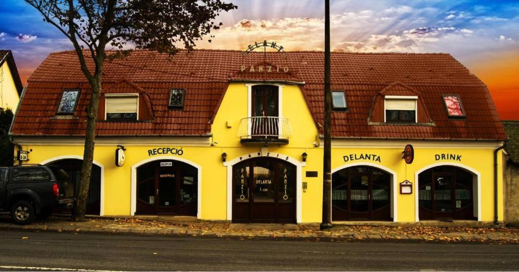 a yellow building with a red roof on a street at Delanta Panzió in Pécs
