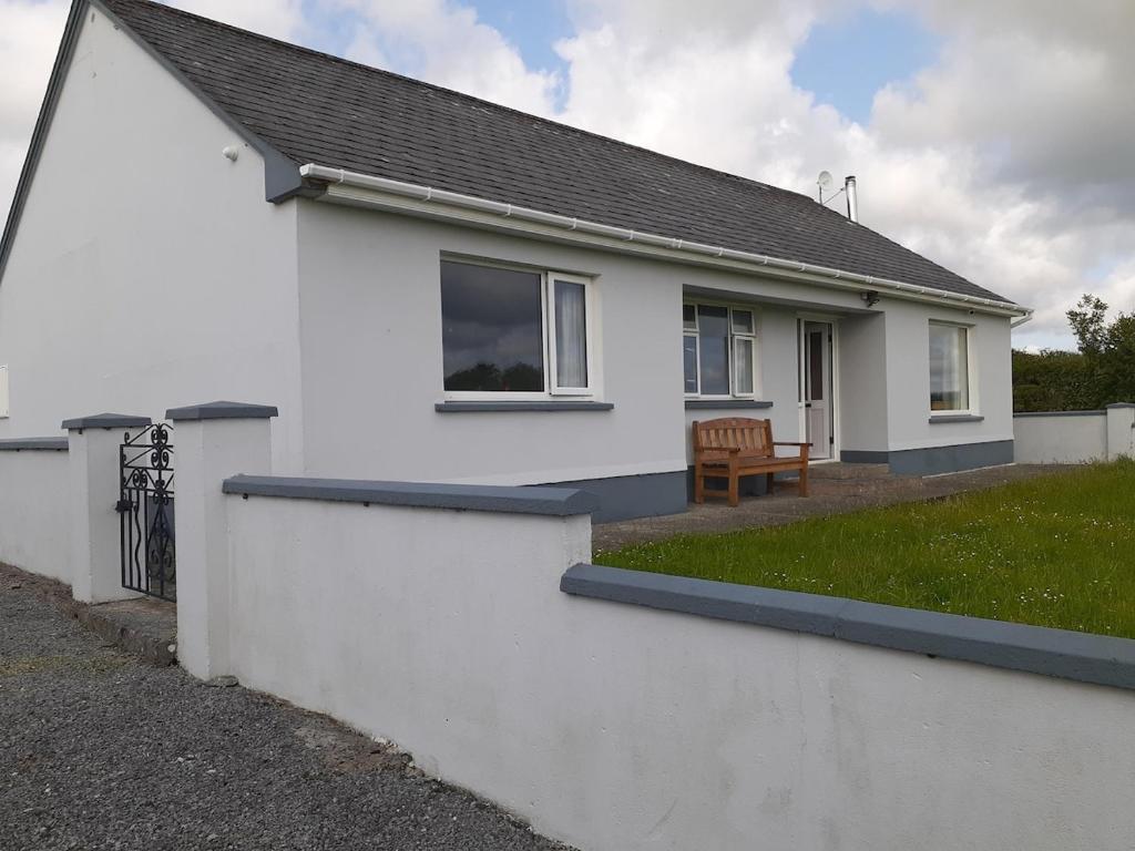a white house with a grass yard in front of it at Meadow View Cottage in Clooncullin Bridge
