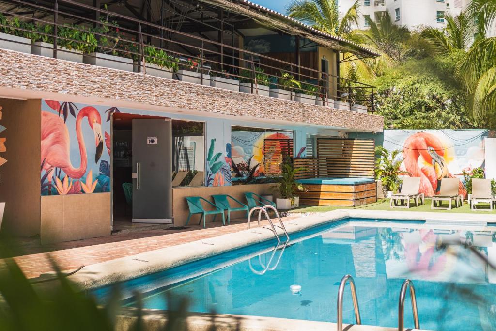a pool in front of a building with a mural of flamingos at The Cantamar Beach Hostel in Santa Marta
