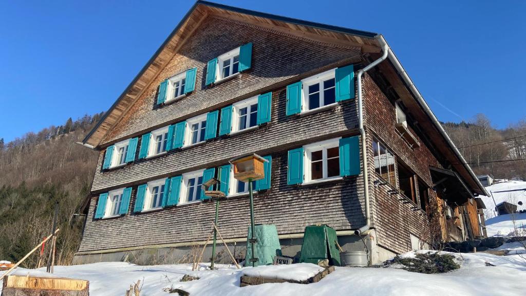 a large wooden house with blue windows in the snow at Berghaus Antonia in Mellau