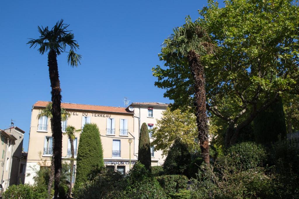 un bâtiment avec des palmiers en face de celui-ci dans l'établissement L'Hôtel du Terreau Logis de France, à Manosque