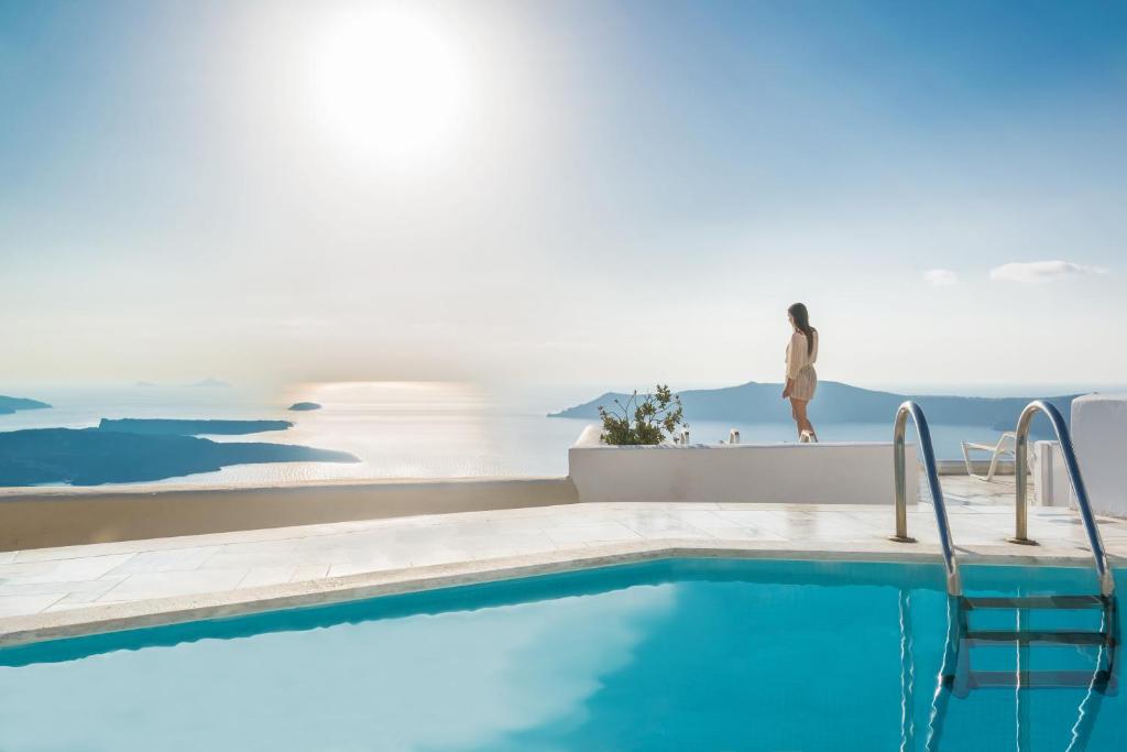 a person standing on a ledge next to a swimming pool at Iliovasilema Hotel & Suites in Imerovigli
