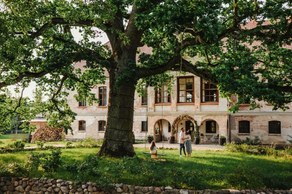 a couple standing under a tree in front of a building at Folwark Wielka Wieś in Główczyce