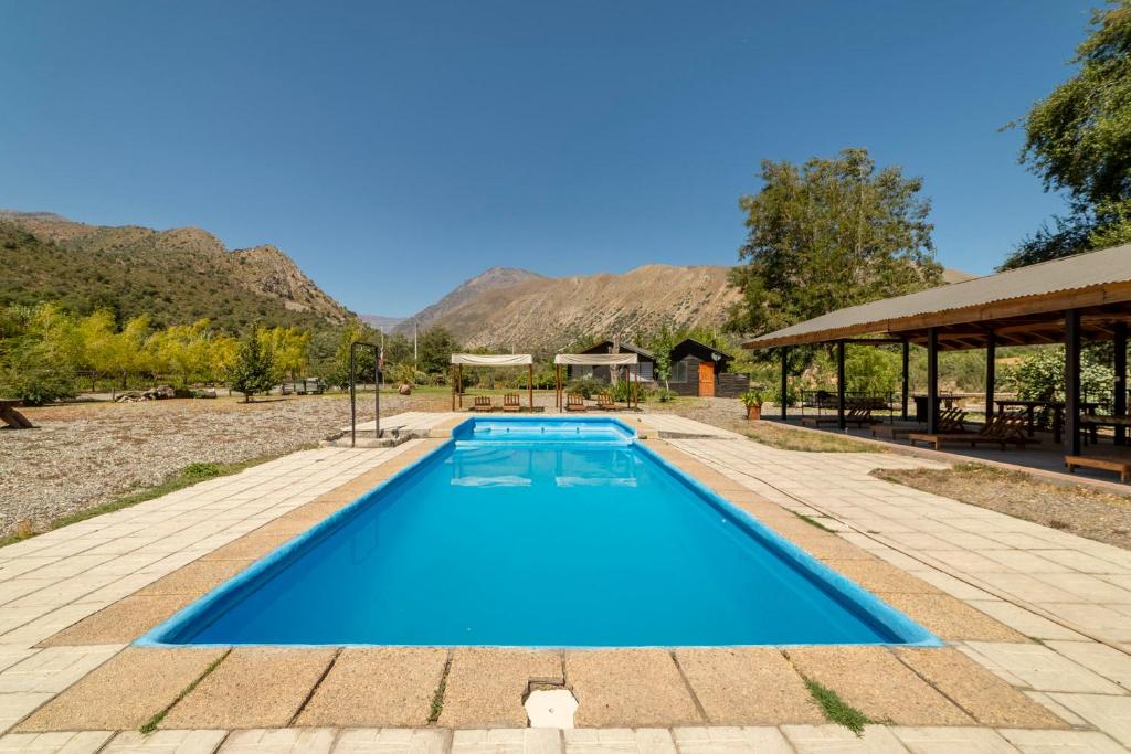 a blue swimming pool with a pavilion and mountains in the background at Cabañas Emporio de la Meme in San José de Maipo