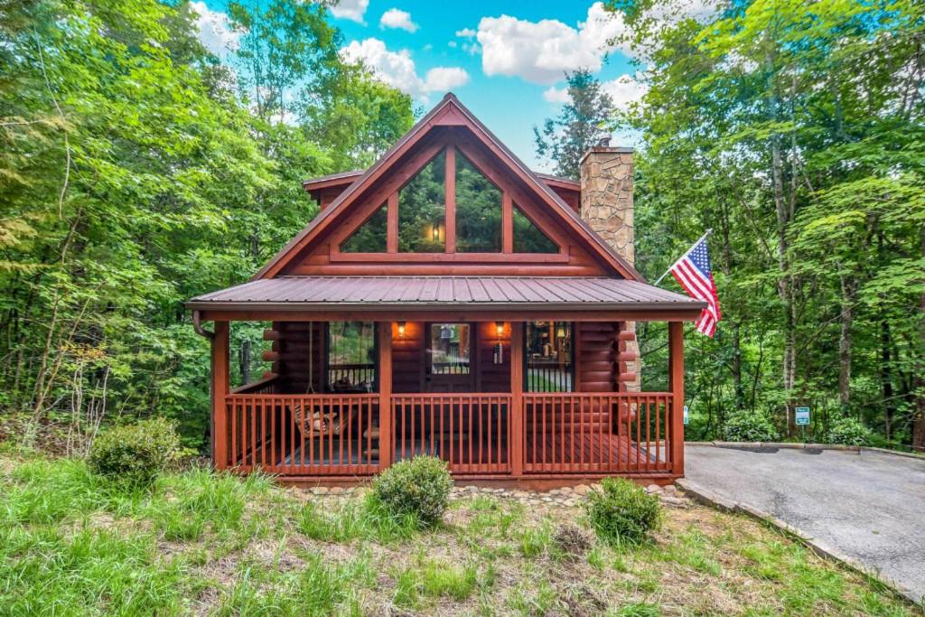 a log home with a wrap around porch and an american flag at Freedom Creek Hideaway-Veteran Host-Pet Friendly-Single nights-Newly Renovated!! in Pigeon Forge